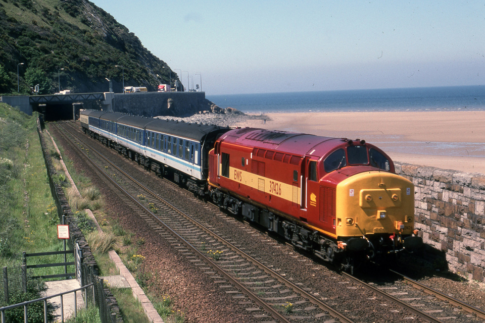 On May 28 1997, former BR 37426, in the colours of private freight operator English, Welsh & Scottish Railways, hauls a rake of Mk 1and Mk 2 coaches, past Penmaenmawr. ROGER SIVITER / COLOUR RAIL